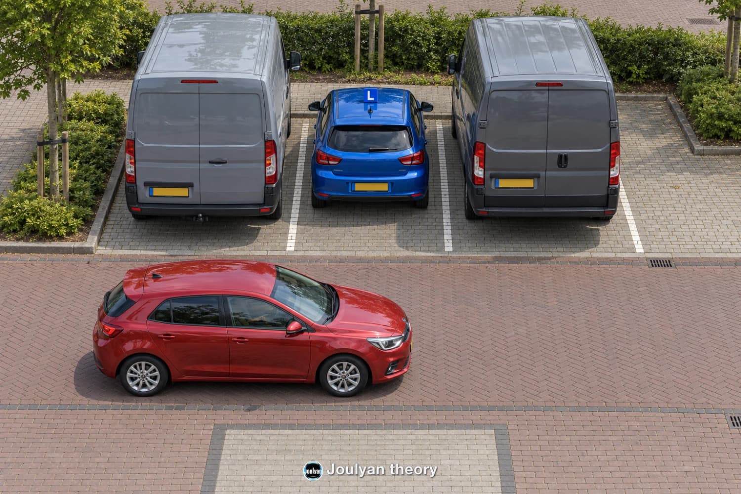 Blue learner car between two grey vans with a red car travelling behind the parking bays